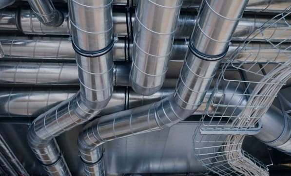 The image shows a network of metal air ducts and ventilation pipes, part of an HVAC system designed for regulating indoor air quality in a commercial or industrial building.